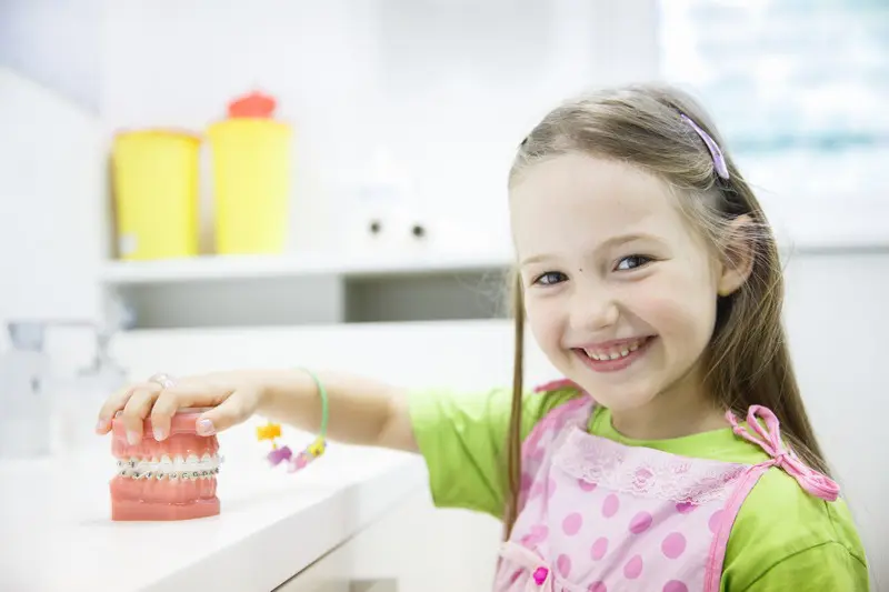 A smiling young girl at Stellar Orthodontics in San Marcos, CA holds a dental model with braces, highlighting children's orthodontic treatment.