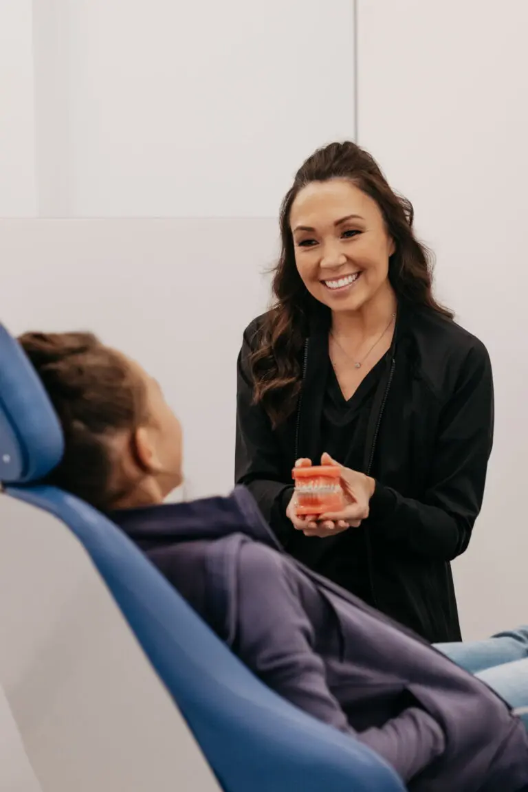 At Stellar Orthodontics in San Marcos CA, a dental professional smiles while holding a dental model and discussing Phase I treatment with a patient in the chair.