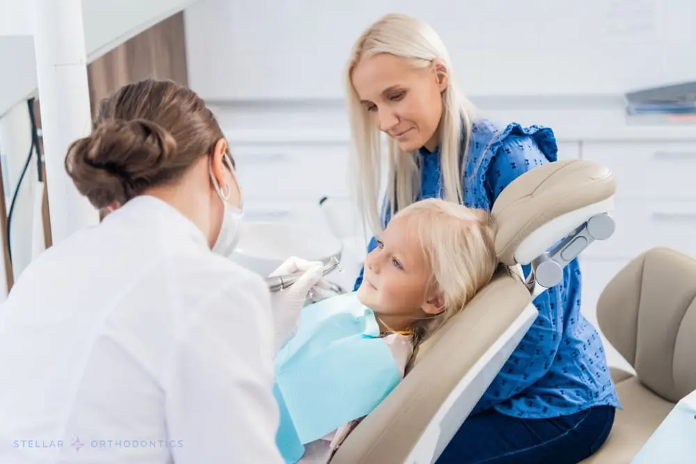 At Stellar Orthodontics in San Marcos, CA, a dentist examines a young girl’s teeth as her mother sits beside her in the modern clinic after being explained about How to Fix Overbite in San Marcos, CA.