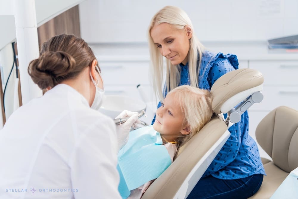 At Stellar Orthodontics in San Marcos, CA, a dentist examines a young girl�s teeth as her mother sits beside her in the modern clinic after being explained about How to Fix Overbite in San Marcos, CA.