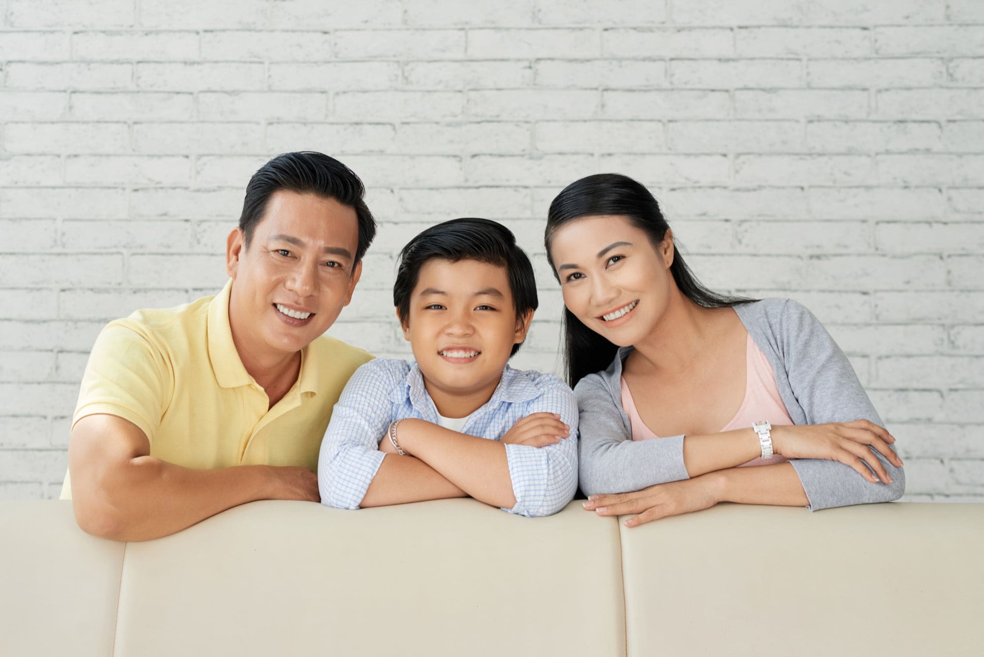 An Asian family relaxes on a couch against a white brick wall, exploring orthodontic choices at Stellar Orthodontics in San Marcos, CA