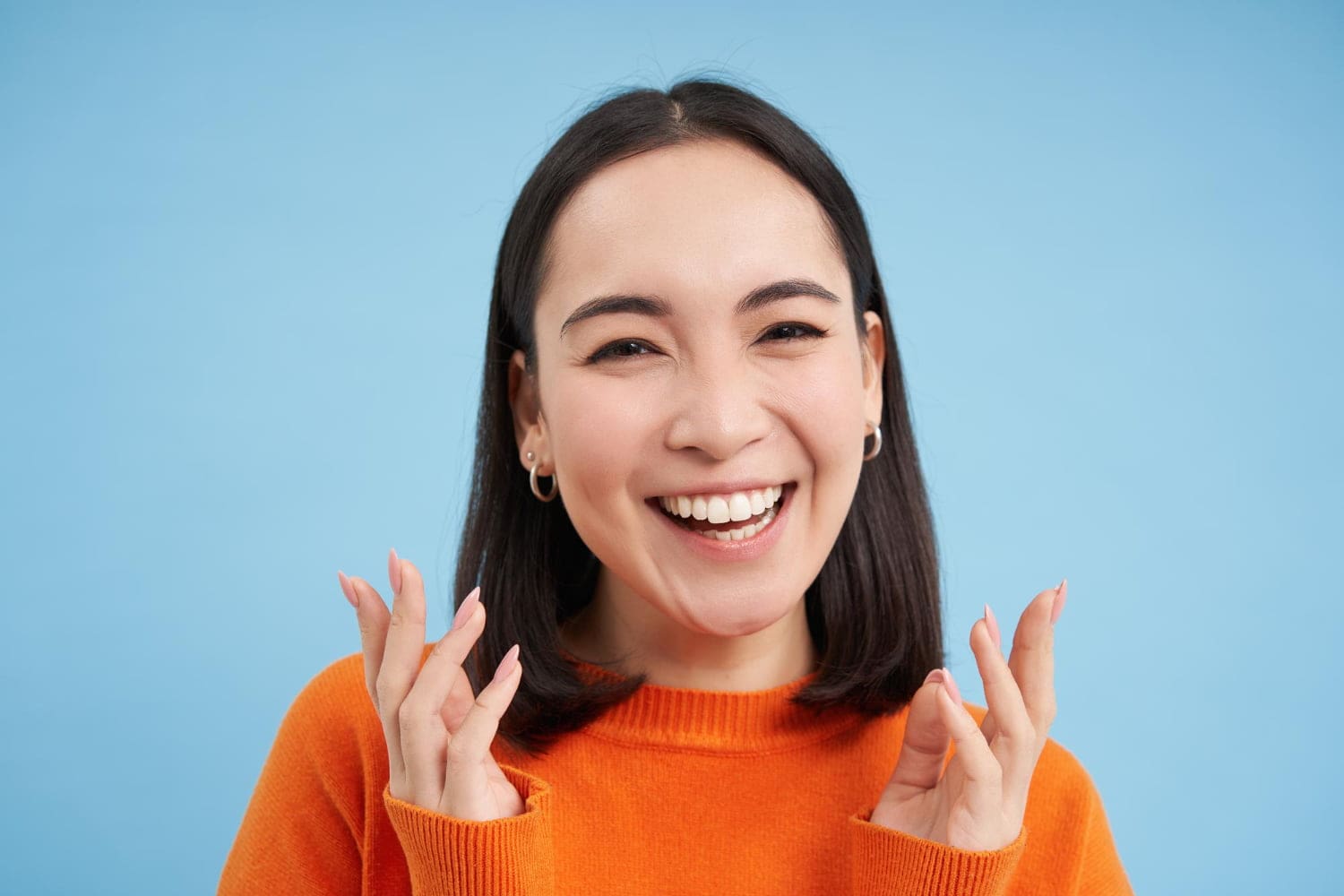 A young woman with straight dark hair and orange sweater smiling show result Invisalign treatment at Stellar Orthodontics in San Marcos, CA.