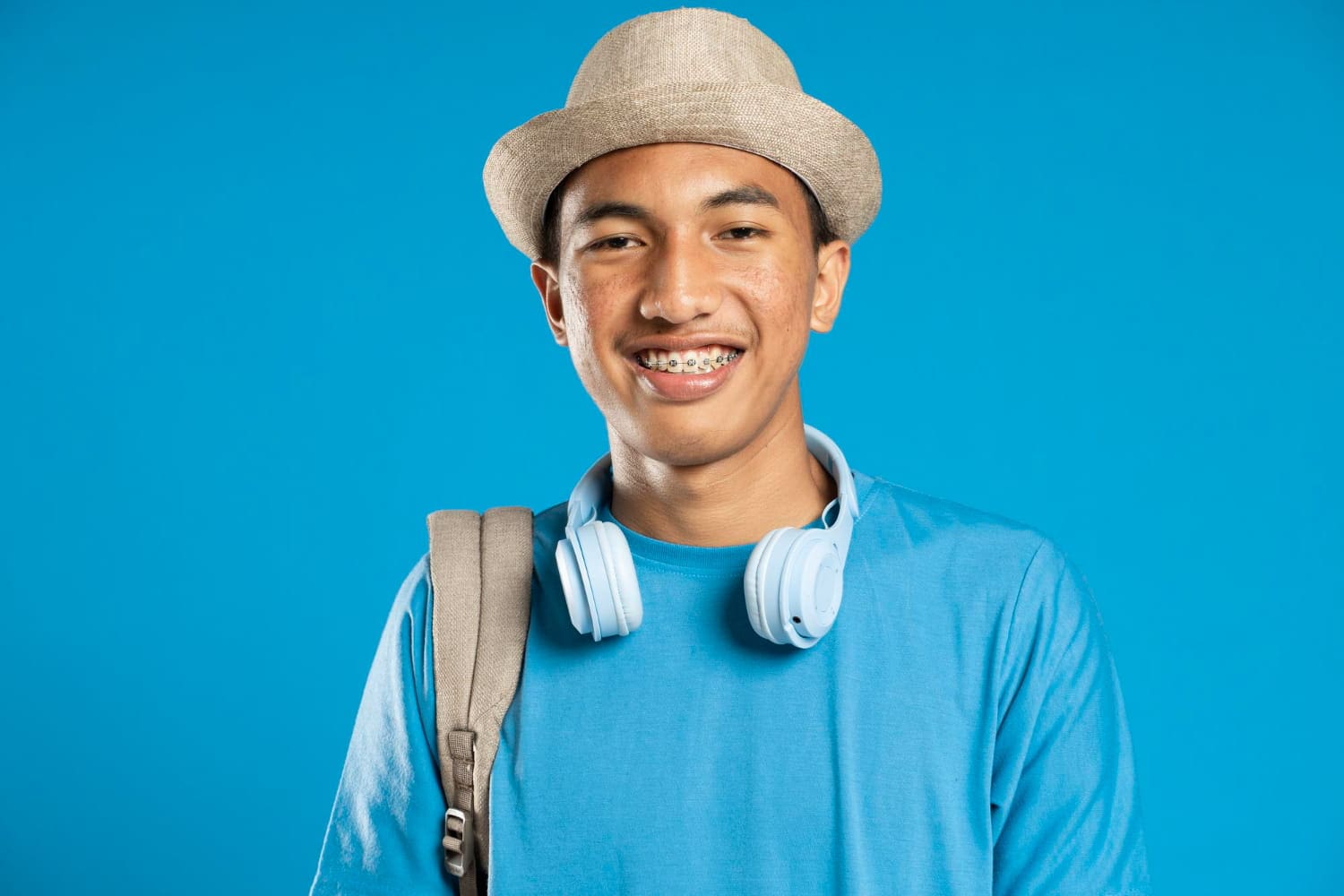 A smiling teen with braces, a hat, a backpack, and headphones represents affordable braces cost at Stellar Orthodontics in San Marcos, CA.