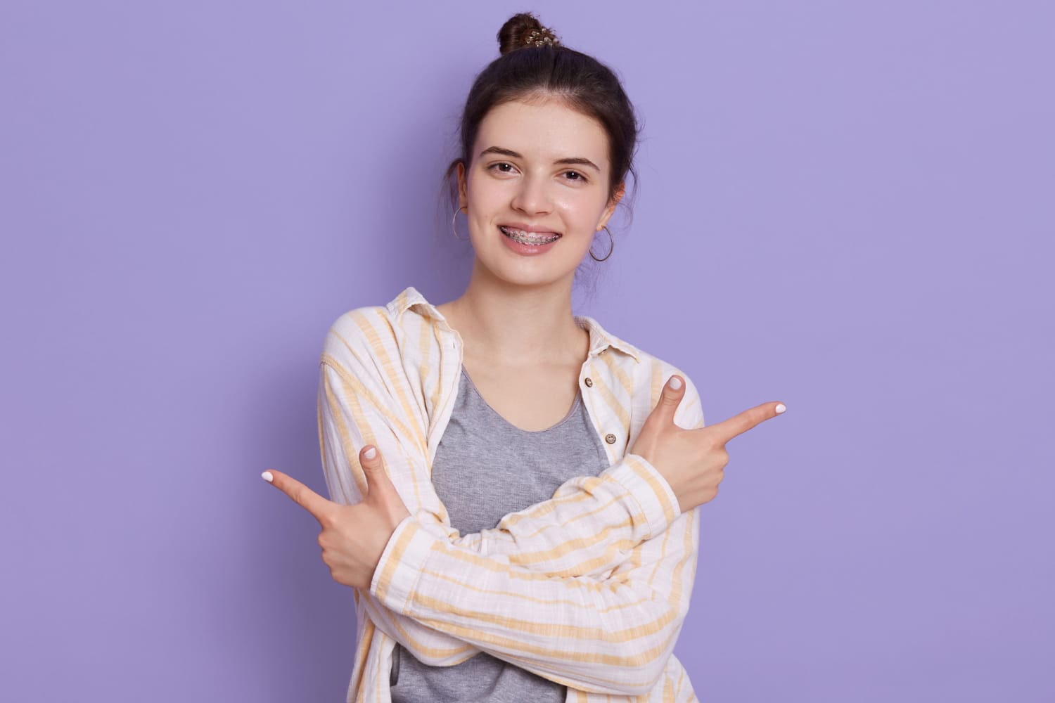Stellar Orthodontics Smiling young woman with braces points sideways, representing affordable braces cost at Stellar Orthodontics in San Marcos, CA.